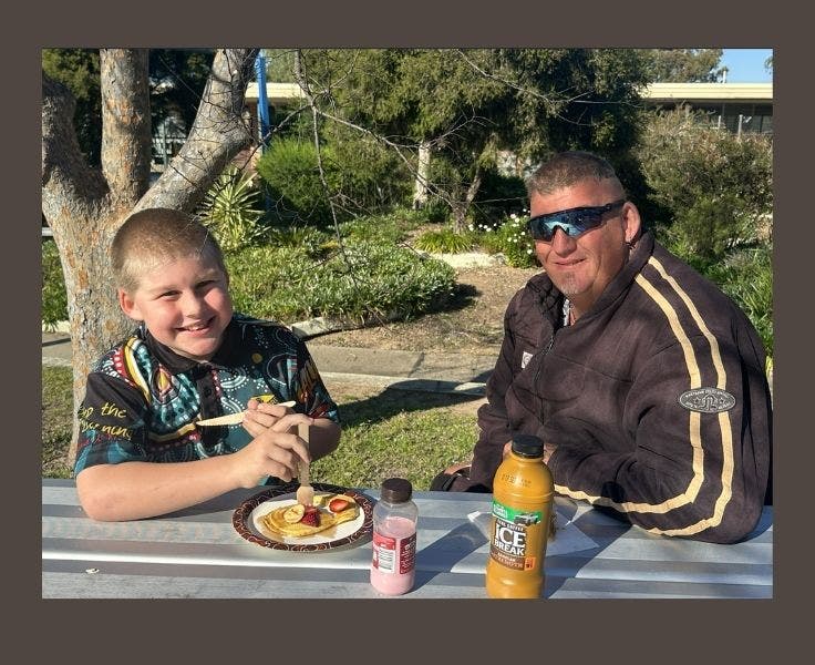 A student and his father seated at a table eating pancakes