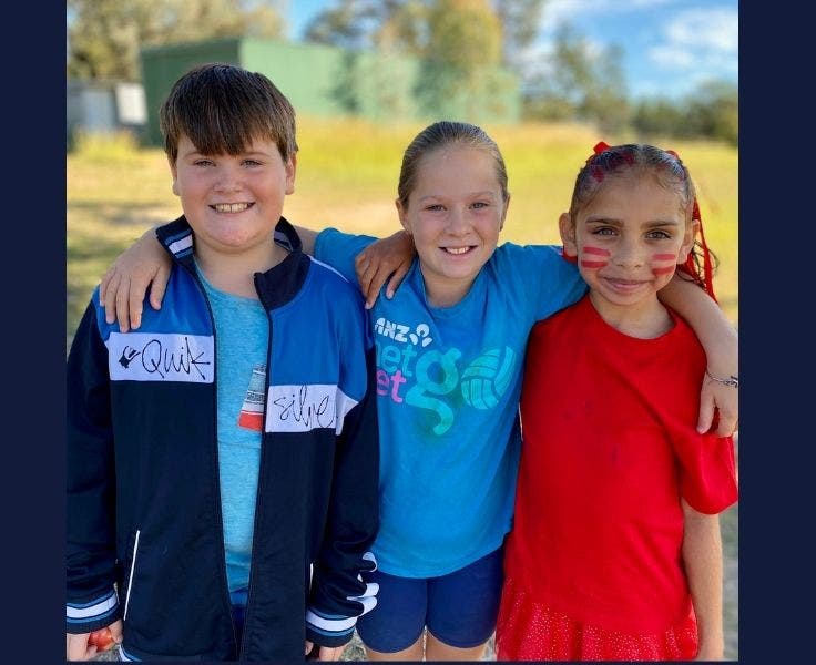Three students standing in a line with their arms on each other's shoulders and the cross country track in the background