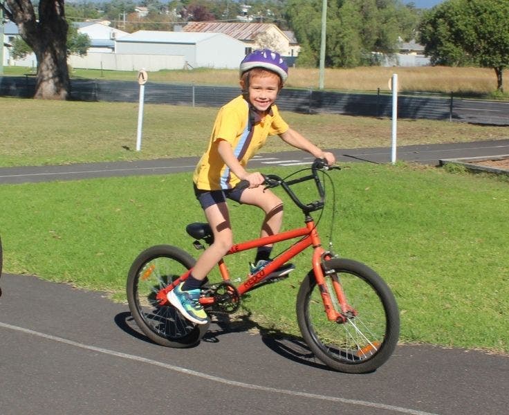 A student riding a red push bike on a tar bike track in the school grounds