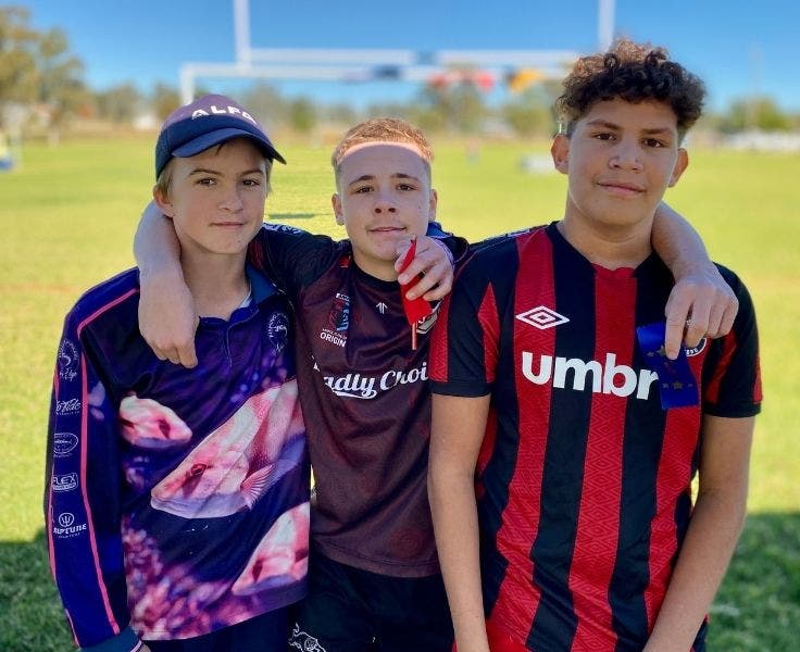 Three students holding ribbons with the athletics field in the background