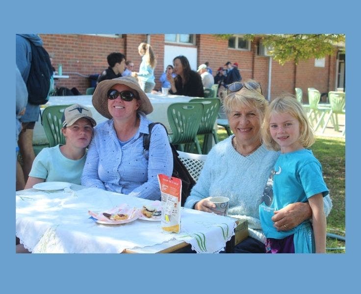 Two students, their mother and grandmother, seated a table with an embroidery tablecloth eating high tea