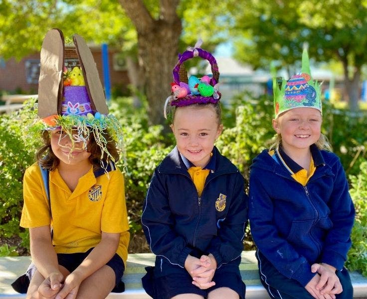 Three students seated on a bench, wearing homemade easter hats