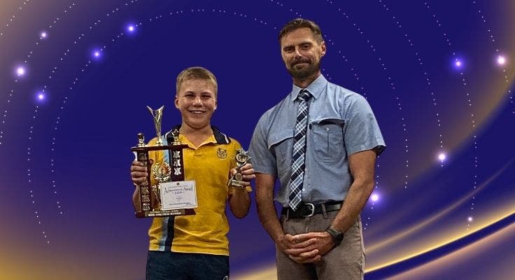A student receiving a trophy from a teacher posing for the camera